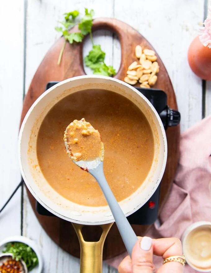 The satay sauce in a pot beginning to curdle at first and a spoon showing how it looks curdled first and that this is normal initially