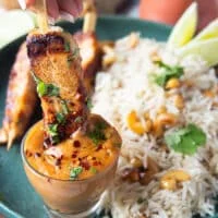 A grilled halibut skewer dipped into a bowl of satay sauce showing how luscious it is