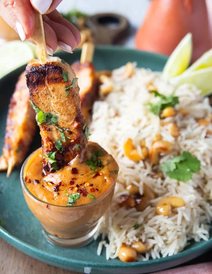A grilled halibut skewer dipped into a bowl of satay sauce showing how luscious it is