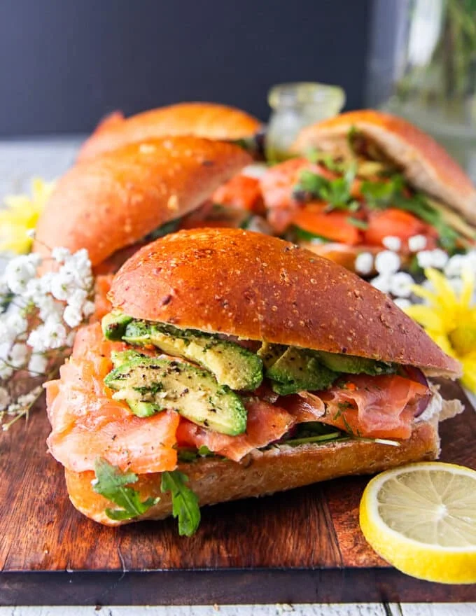 One smoked salmon sandwich on a board showing the layers of fillings and toppings close up surrounded by lemon slices