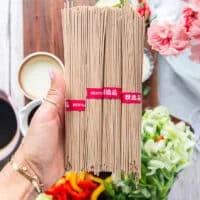 A hand holding a bunch of soba noodles showing how they look close up, raw and uncooked with the toasty color