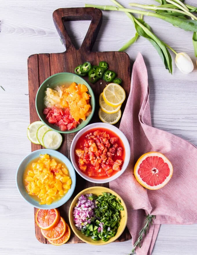 ingredients needed for citrus salsa including: segmented grapefruit, segmented oranges, blood orange, lemon, some diced onions in a bowl, diced jalapenos in a bowl, and minced cilantro in a bowl and salt