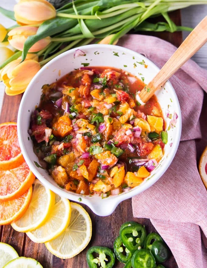 a bowl of citrus salsa with a spoon surrounded by citrus slices