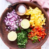The ingredients for pineapple salsa are finely diced in a large wooden bowl