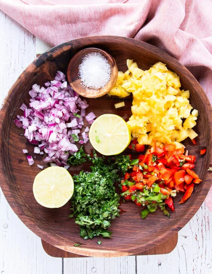 The ingredients for pineapple salsa are finely diced in a large wooden bowl