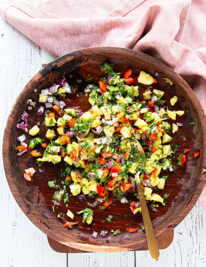 All the pineapple salsa ingredients are tossed and mixed well in a large wooden bowl and seasoned.