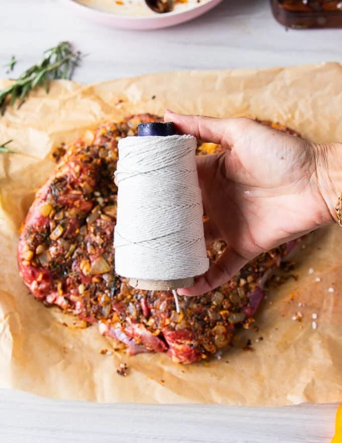 A hand holding a kitchen twine to begin tying up the boneless leg of lamb for roasting