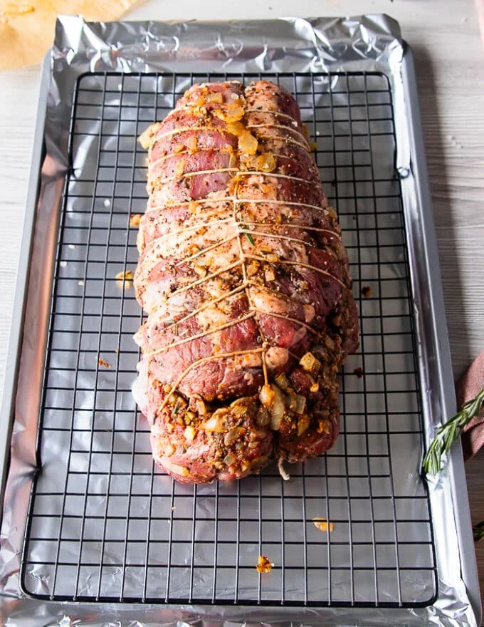 The tied up boneless leg of lamb is placed over a wire rack over a baking sheet and ready to marinate or begin roasting