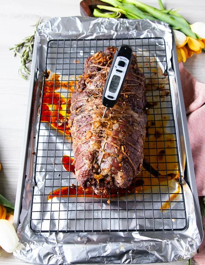 The slow roasting of the boneless leg of lamb is completed the first half at low temperature and a meat thermometer is showing the perfect temperature