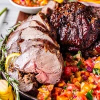 close up of roasted boneless leg of lamb on a bed of citrus salsa surrounded by fresh rosemary