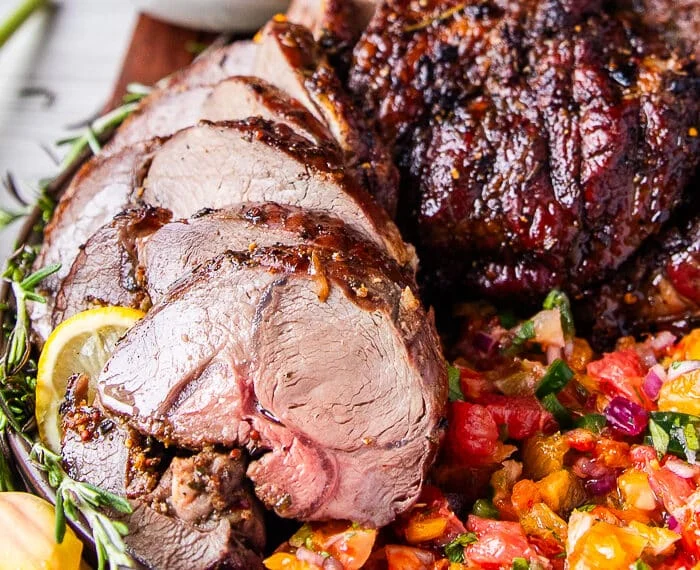 close up of roasted boneless leg of lamb on a bed of citrus salsa surrounded by fresh rosemary