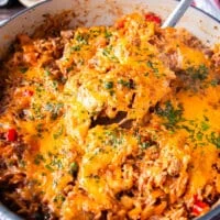 A spoon taking out a portion from the stuffed peppers casserole to serve on a plate showing the stretchy cheese