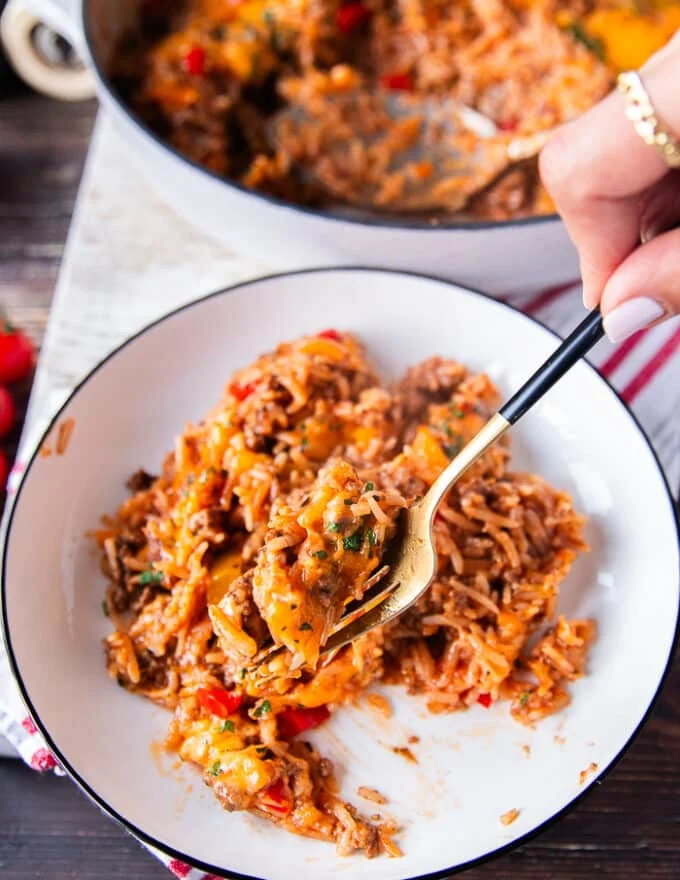 A portion of the stuffed pepper casserole on a plate and a fork eating it showing close up the fluffy rice