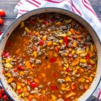The tomatoes and stock is added to the skillet to cook the stuffed peppers casserole.