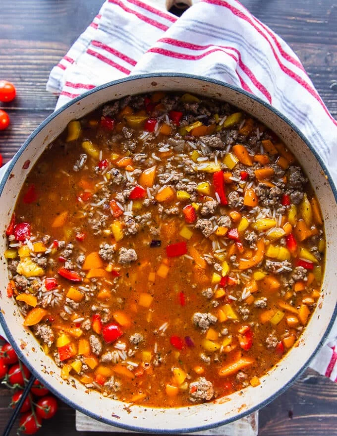 The tomatoes and stock is added to the skillet to cook the stuffed peppers casserole.