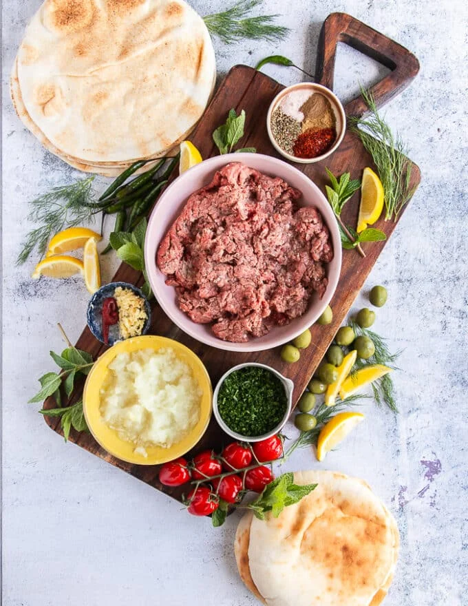 Arayes Ingredients: a bowl of minced lamb or beef or combo, bowl of minced onions, a bowl of minced herbs, a bowl of minced garlic, a bowl of tomato paste, a plate of seasoning spices, a variety of pita breads