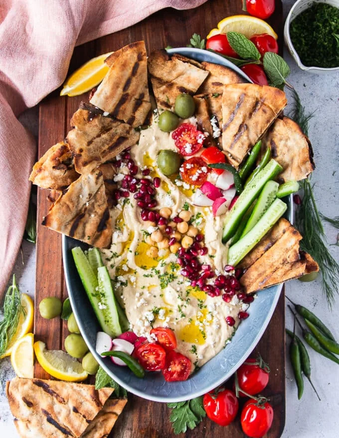 A plate of meat stuffed pita arayes made with thin pita bread as a variety and served with hummus, cucumbers, lemon, pomegranate arils and lemon wedges