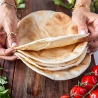A hand holding a stack of thin pita breads to show what they look like