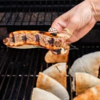 Arayes cooked on the grill and a hand holding the arayes showing the grill mark before flipping and grilling