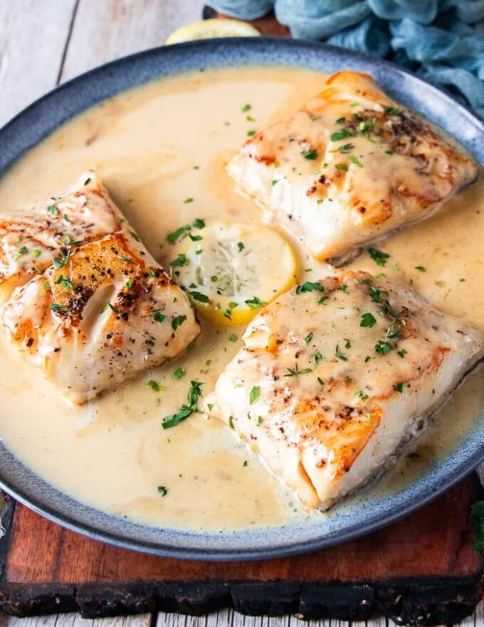 A plate of fully plated black cod in a creamy lemon beurre blanc sauce.