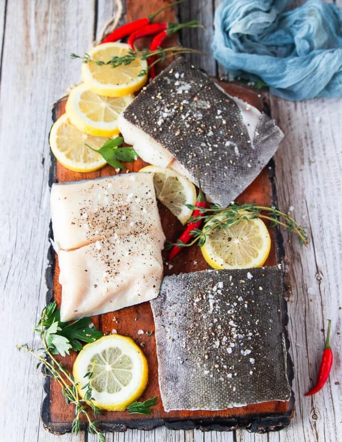 Black cod fillets seasoned on both sides with salt and pepper on a wooden board