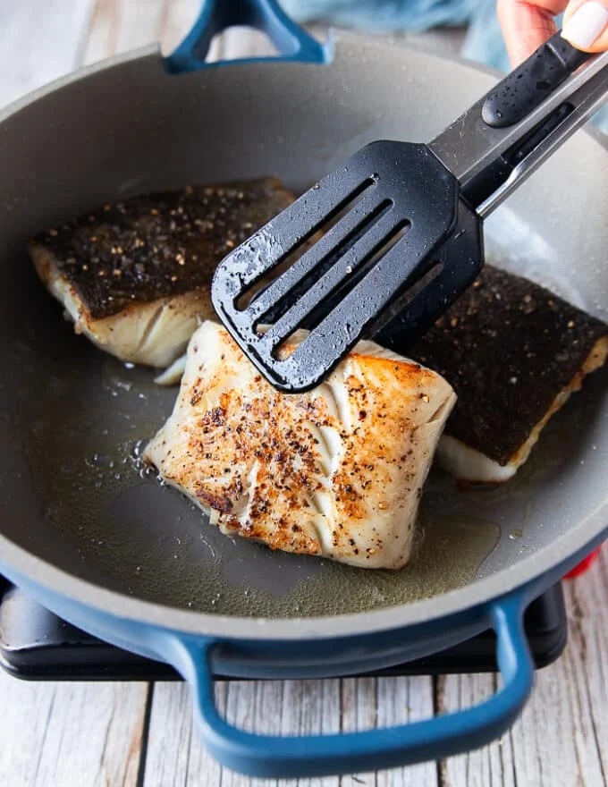 Flipped and golden black cod fish in the skillet ready to be removed
