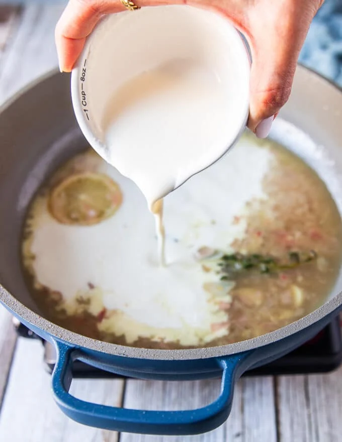 A hand pouring the cream over the shite wine sauce to finish the beurre blanc or creamy lemon sauce for black cod recipe