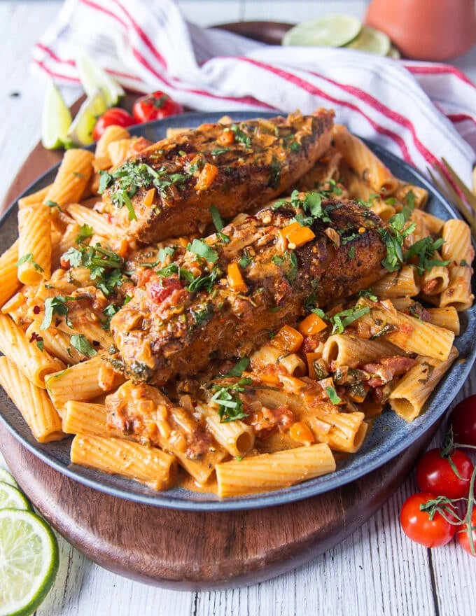 Plated cajun pasta with cajun fish or chicken on top served on a plate and plenty of fresh cilantro