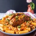 A plate of cajun pasta with plenty of cajun sauce and topped with a cajun halibut for extra protein surrounded by a vase with flowers
