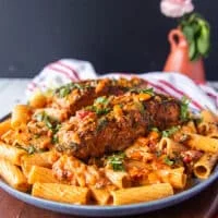 A plate of cajun pasta with plenty of cajun sauce and topped with a cajun halibut for extra protein surrounded by a vase with flowers