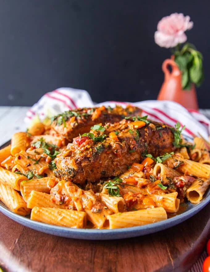 A plate of cajun pasta with plenty of cajun sauce and topped with a cajun halibut for extra protein surrounded by a vase with flowers