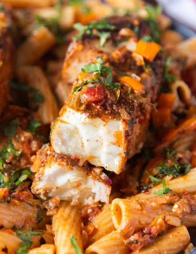 Very close up of a pieces of halibut cut in half over succulent creamy cajun pasta