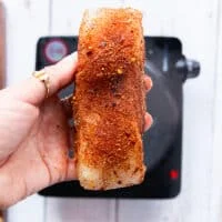 a hand holding cajun seasoned fish or chicken on both sides