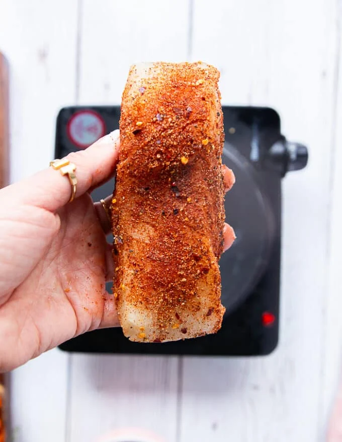 a hand holding cajun seasoned fish or chicken on both sides