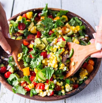 Corn and Tomato Salad in a large wooden bowl with two wooden spoons