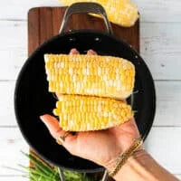 a hand holding a cleaned corn on the cub with rusks and hair removed and optionally cutting it in half