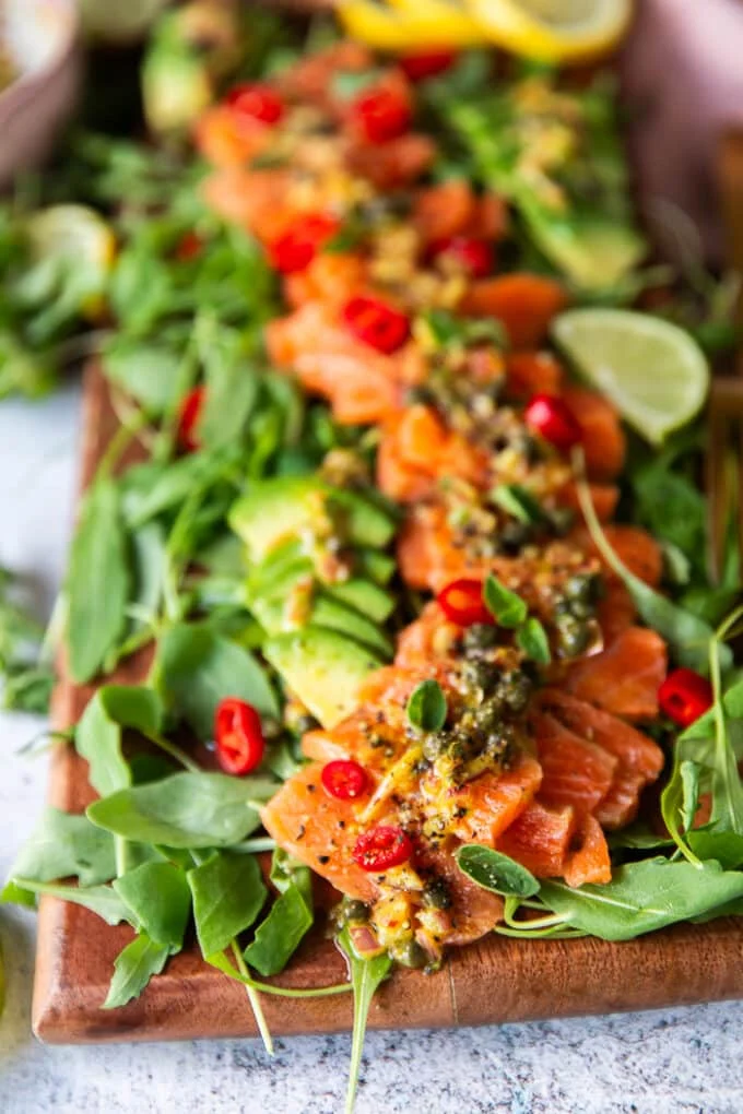 closeup of a board with arugula and salmon carpaccio over it and avocado slices around it