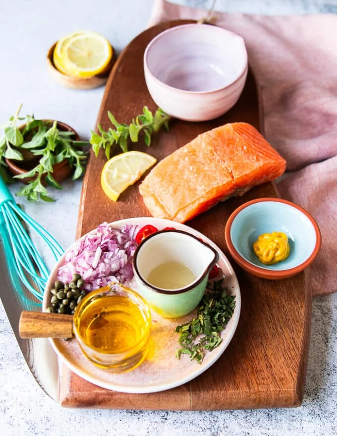 Ingredients for salmon carpaccio including sushi grade salmon, mustard in a bowl, olive oil in a cup, some capers in a bowl, shallots in a bowl some herbs minced, some lemon juice in a bowl , salt and pepper