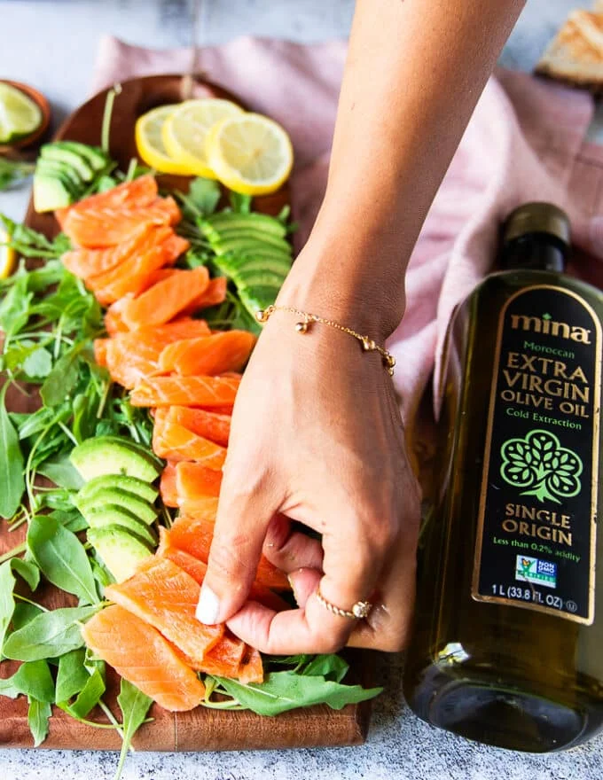 a hand arranging the thinly sliced salmon over a bed of arugula