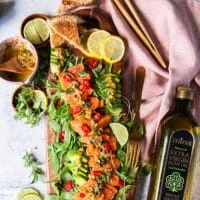 A top view full plate of salmon carpaccio with some pita chips on the side, some avocado slices with the salmon and lemon slices for garnish