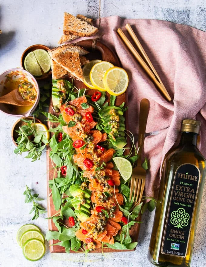 A top view full plate of salmon carpaccio with some pita chips on the side, some avocado slices with the salmon and lemon slices for garnish
