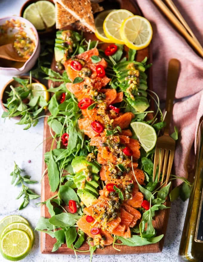 A large board with salmon carpaccio with capers and dressing