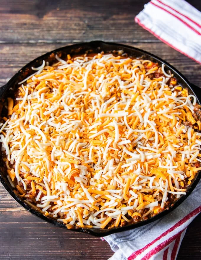 Cheese is sprinkled over the taco spaghetti in the cast iron and it's now ready to bake