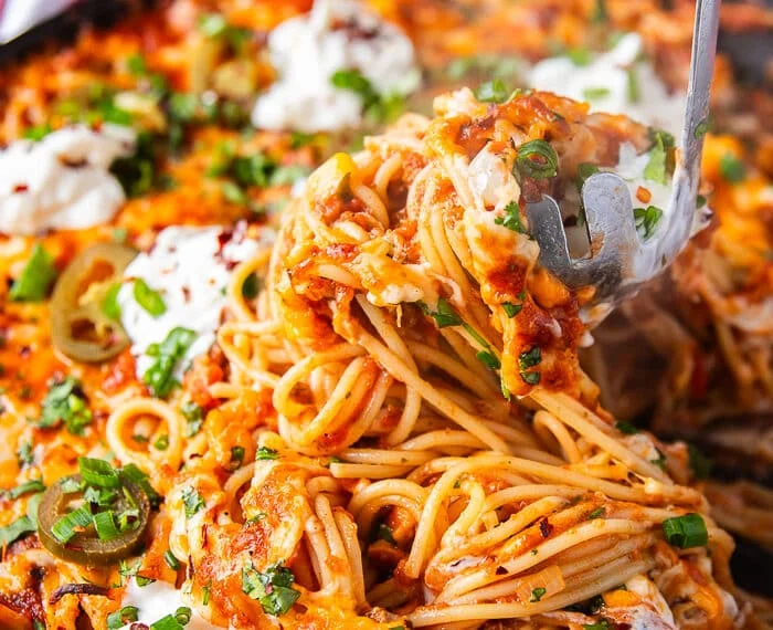 A pasta spoon scooping up some taco spaghetti from the pan showing the stretch of cheese with spaghetti with the taco meat and sauce