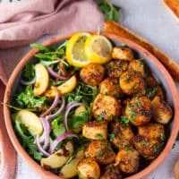 A plate of broiled scallops served with lemon slices and a side of salads