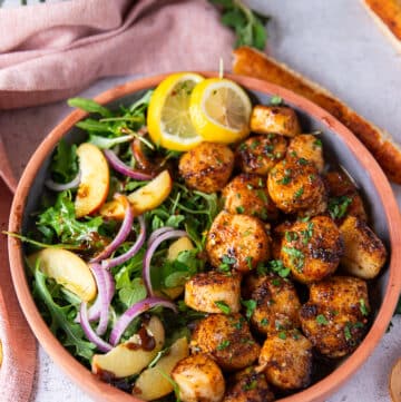 A plate of broiled scallops served with lemon slices and a side of salads