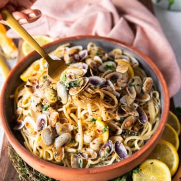 A fork stretching the clam pasta showing the details of the spaghetti and the cooked clams in the simple clam sauce with some lemon slices and chilli flakes