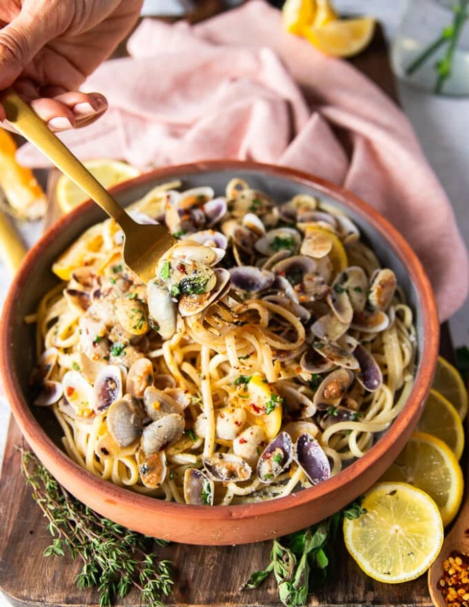 A fork stretching the clam pasta showing the details of the spaghetti and the cooked clams in the simple clam sauce with some lemon slices and chilli flakes