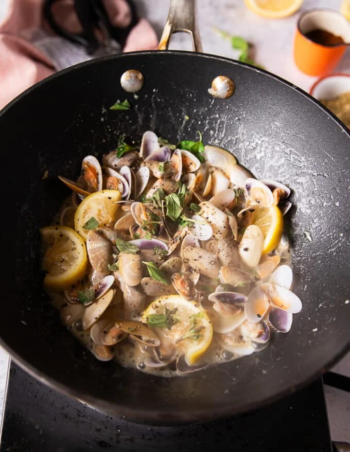 The clams are added and starting to exude some water and create a sauce in the pan