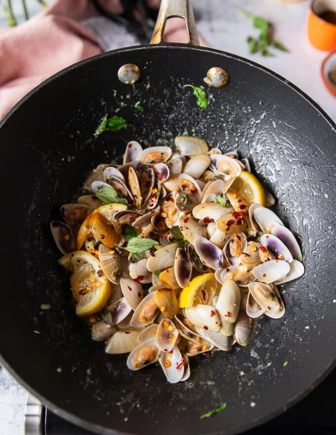 fully cooked clams in a skillet with lemon slices, garlic and chilli flakes, all clams have opened and cooked and ready to make clam pasta